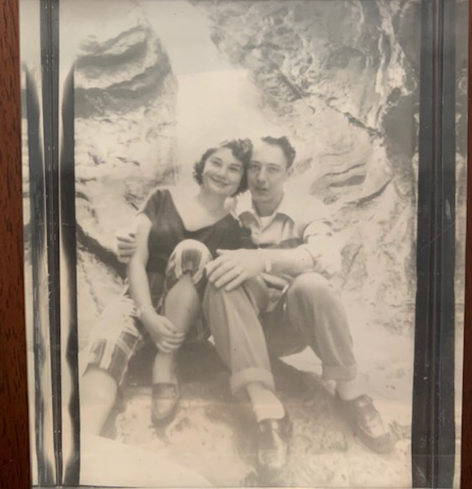 black and white photo of my mom and dad. They are sitting, my dad's arm around my mom, in front of a bunch of rocks.
