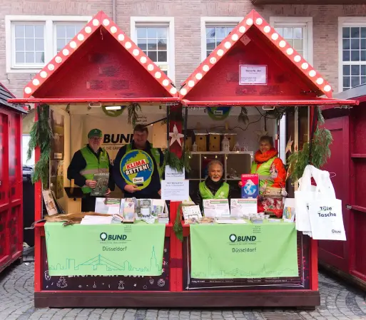 Frontales Foto von der Weihnachtshütte. Vier BUND-Aktive befinden sich in der Hütte und schauen freundlich in die Kamera. (Foto: www.mutbuergerdokus.de)
