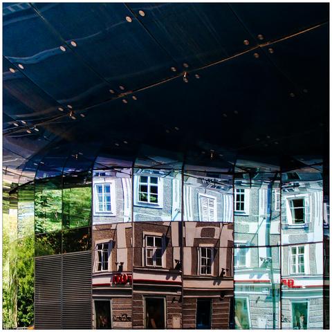 Facade of a blob architecture-style building with reflections from residential buildings.