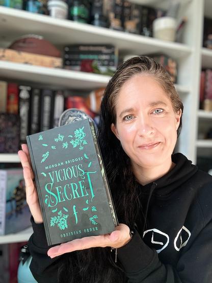Ich halte folgendes Buch vor meinem Bücherregal in meinen Händen:

Vicious Secret
aus der Reihe Obsidian Order
von Morgan Bridges
vom Verlag Penguin Random House

Ich zeige das Cover. Es ist dunkelgrau mit grüner Schrift.