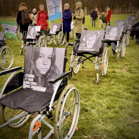 Five (out of hundred) wheelchairs in a row, each with a BW photo of a longcovid or other PAIS patient who could not attend, on the Malieveld in The Hague, The Netherlands
