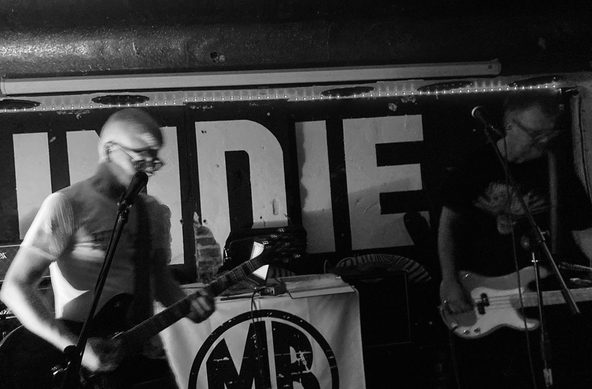 Zwei Männer spielen Gitarre und Bassgitarre auf einer Bühne.