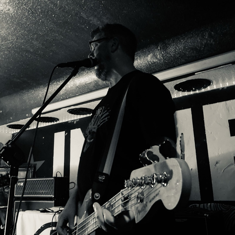 Ein Mann spielt Bassgitarre auf einer Bühne und singt in ein Mikrofon.