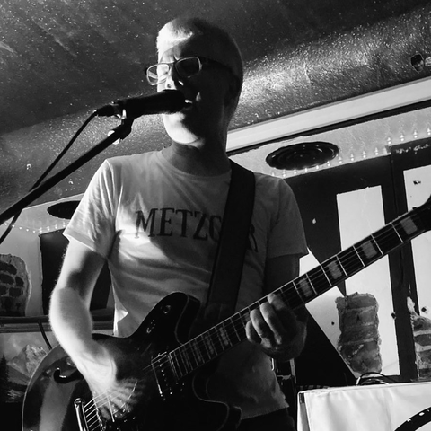 Ein Mann spielt E-Gitarre auf einer Bühne und singt in ein Mikrofon.