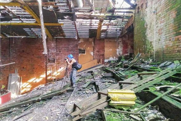 Photo of girl taking a photo, with a camera on a tripod, inside a collapsing building