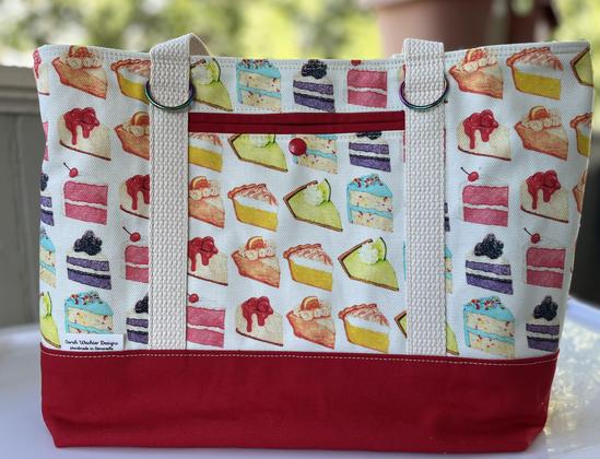 A tote bag with a red canvas base and white background, printed with large slices of cake and pie in rainbow gradients. It is very gay and very tasty looking.