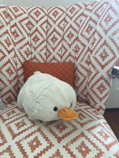 White stuffed duck leaning against an orange pillow on a chair upholstered in orange and white diamonds