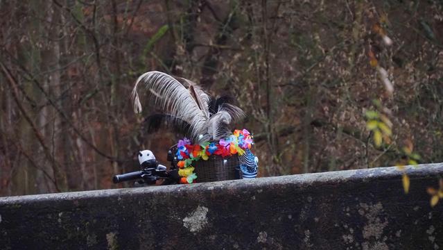 Der Lenkerkorb mit Federn bunten Blumengirlande und Lichterkette, schaut über ein Betonbrückengeländer hinweg