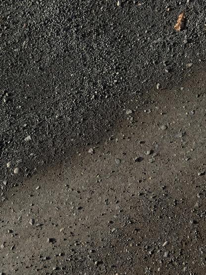 A dry, gravel surface with small rocks and a single brown leaf. Strong side shadows and ombré brown colors