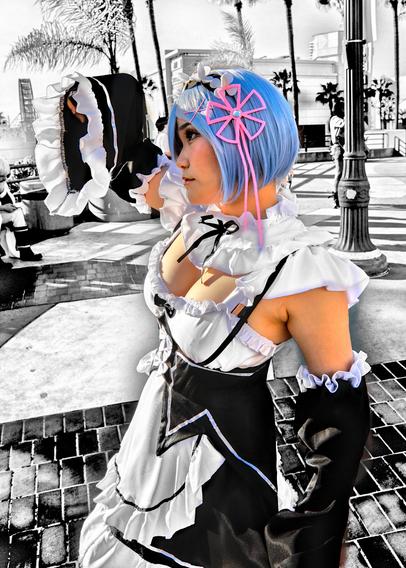 Cosplayer Peachtgummy as Rem from the game Re:Zero.  She's wearing a maid outfit and showing healthy cleavage and some armpit.  The image is in selective coloring highlighting the blue hair and pink ribbon.  The maid outfit is in traditional black and white with heavy tonal editing.