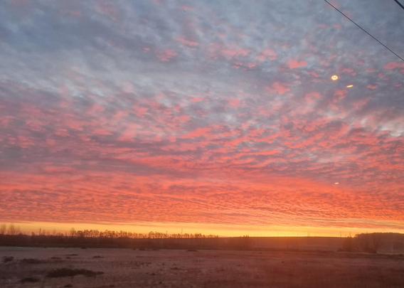 Photo du ciel à l'aube, prise depuis le train. Le soleil levant derrière l'horizon peint les nuages en orange, rouge et rose.