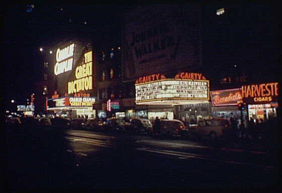 This image depicts a vibrant scene from Times Square at night, showcasing the iconic theaters such as the Gaiety and Astor. Brightly illuminated signs advertise various shows like "The Great Dictator" starring Charlie Chaplin and other attractions in red neon lights against the dark backdrop of the city streets. The atmosphere is bustling with activity; people can be seen walking along the sidewalks while cars drive by on the street below, contributing to a lively urban nightlife ambiance typical of Times Square during that era.

Additional context for this image includes its historical significance as captured through Gottscho-Schleisner's work in 1940. This photograph is part of their extensive collection documenting New York City views and reflects an important aspect of the city's cultural landscape from a bygone period, offering insight into entertainment offerings at that time and providing visual evidence for historical research.

The image source includes metadata indicating its origin: Gottscho-Schleisner, Inc. with the reference number 691e/843f5a2c0d74ef12bea2bb2b.jpg found in an archive from a private collector or institution specializing in historical photography and documentation of New York City scenes.