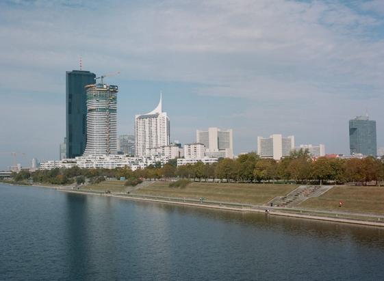 Blick auf die Skyline von Kaisermühlen von der Donauinsel aus. Mit der Sonne im Rücken werden die Fassaden gut ausgeleuchtet. Die UNO-CITY verschwindet hinter den Neubauten und alte Antennenspitzen der Hochhäuser, die montiert worden sind, um besonders hoch sein zu können, wirken etwas verloren auf den niederen Stockwerken. Früher hätte ich gesagt, sieht aus wie eine Raumstation. Aber das stimmt nur für den Gemeindebau, der unten am Donauufer herumgrundelt. Die hoch gezogenen Türme sind nur heiße Luftschlösser.