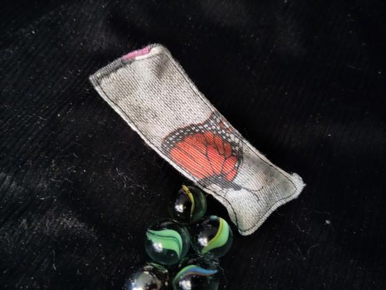 Un rectangle de tissus avec un papillon dessus et des billes devans. On vois qu'il y a une bille a l'intérieur du tissus