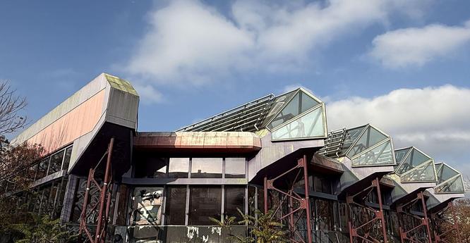 Brutalistische Betonarchitektur mit mehreren Glasdächern und Metallstützen unter bewölktem Himmel. Foto: Eike Roswag-Klinge