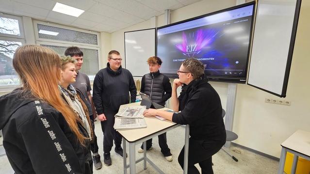 Gruppe junger Menschen vor einer Tafel mit dem Logo "EJZ" und Schrift, vermutlich in einem Schulraum.