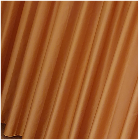 Monochrome shot of an orange curtain. The gently shimmering folds fall in even waves. Their direction, slightly slanted from top right to bottom left, creates a lively movement. The incidence of light forms ridges and valleys. A small piece of parquet flooring can be seen in the bottom left corner. An atmosphere full of movement, joy and anticipation.