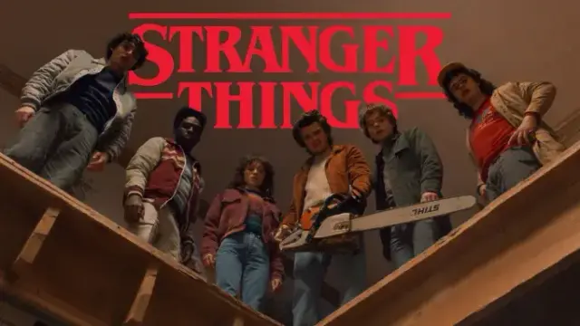 Promotional image for Stranger Things Season 5 showing the main cast of seven young adults standing in a line, shot from a low angle looking up. They're holding weapons including a chainsaw and baseball bat, wearing 1980s clothing. The show's distinctive red logo with parallel lines appears at the top against a beige/brown background.