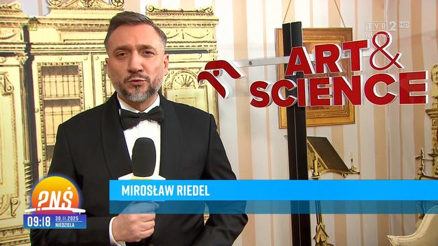 Dziennikarz TVP Mirosław Riedel (podpisany na belce) obok czerwonego logotypu ORLEN ART & SCIENCE, w jednym z pomieszczeń w Teatrze Wielkim, na tle jakiejś złotej szafy.