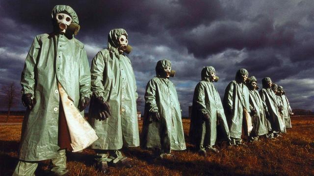 A photograph showing many people standing in a row dressed in green plastic long coats, gas masks and head coverings. These are the nuclear biological chemical warfare (NBC) protective outfits in the USSR 1989.