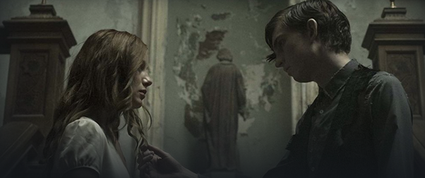 Gothic Horror film The Lodgers: Edward (Bill Milner) touches his sister Rachel's (Charlotte Vega) hair with his head cocked to one side, just staring at her. They are standing on the staircase, and a statue is in the background between them, with its back to the viewer, facing the wall where the paint and plaster are coming away to reveal the fabric of the building beneath. The colours are extremely muted, almost greyscale, with brown as the stand-out dark colours (the bannisters, their hair) and the whole scene seems washed in shades of grey-blue/green.