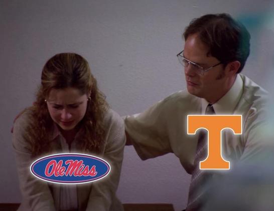 This is a medium shot capturing two people. The Pam from The Office on the left has long, curly hair and is wearing a white button-down shirt, appearing to be in distress or concentration. To the right is Dwight from The Office with short dark hair wearing a white button-down shirt and glasses, leaning in and gesturing with a hand. The image is dominated by white and includes the logo of “OleMiss” in a red oval shape with white lettering in the lower left corner. In the upper right corner is a large orange capital letter "T”. Dwight is comforting Pam, because Lane Kiffin also left Tennessee.