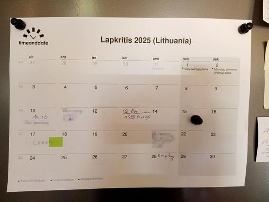 A monochrome printed A4 calendar consisting of one sheet per month, held with magnets to a fridge. A black magnet indicates the current date. Some appointments are written on it in ballpoint pen. One is written on a movable sticker. The calendar has pre-printed holidays and week numbers and is in Lithuanian language.