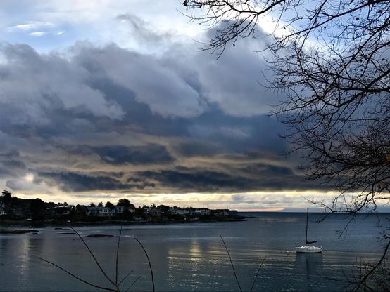 Early morning at local quiet Bay with dramatic clouds with sunlight, reflecting from bottom of cloud layer. Above the low lying cloud is scattered cloud in a blue sky.