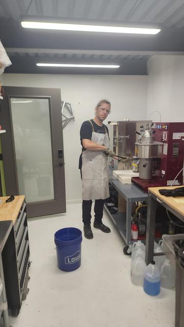 Duane clasps a hot flask with heavy duty tongs, ready to quench it in the bucket of water on the floor.