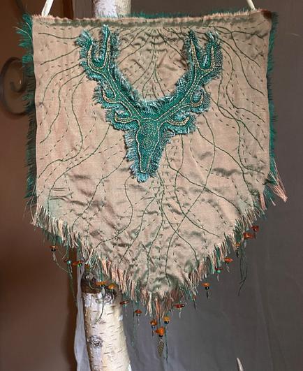 Shot woven gold silk with curving lines of embroidery, embellished with a stag embroidered in gold thread on green fabric. The edges of all fabric are frayed, and the piece is edged with dangling beads of amber and green glass, and tiny brass leaf charms.