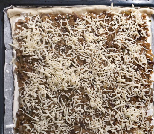 Der belegte Zwiebelkuchen auf dem Blech vor dem Backen