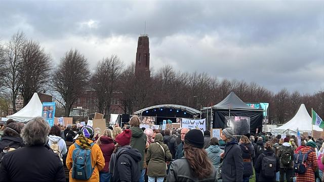 Grote groep demonstranten voor een podium op het Malieveld in Den Haag. Er zijn enkele tenten te zien langs het podium. De demonstranten staan allemaal met de rug naar de camera.