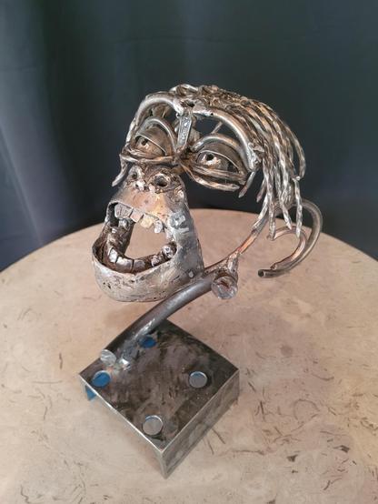 Une tête de bébé singe bonobo en rebut d'acier est placée sur un socle carré. Il a un large sourire et il regarde dans les air.

La tête est incomplète, les éléments suivants sont reconnaissables: la bouche et son nez, les yeux, le dessus de tête et les oreilles.