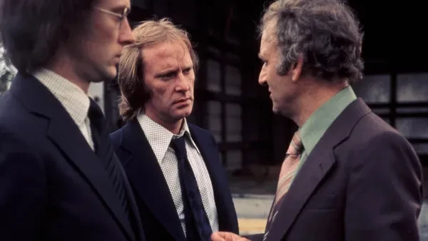 A still from the third series of The Sweeney. Three white men with 1970s-style cheap suits and haircuts talk in the street.