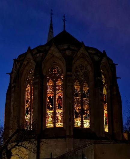 A French Gothic style Victorian church in Glasgow with its stained glass windows glowing as night falls around it.