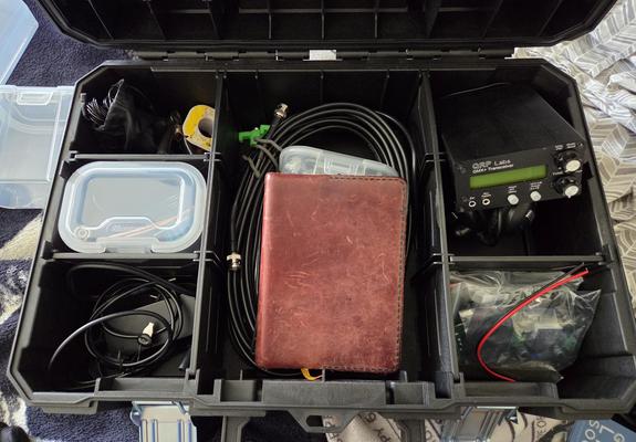 Interior,  tool bin with antennas,  feed line,  little plastic bins of sub components,  batteries,  AC power supply,  and an actual radio transceiver. Handmade leather notebook completes the ensemble.