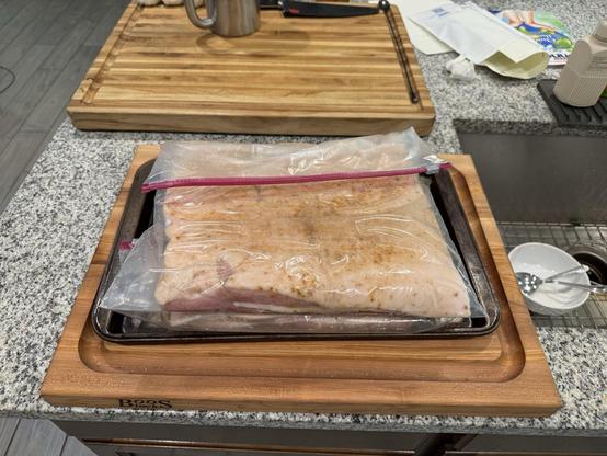 Two halves of a pork belly each sitting in a big zip lock bag on a small baking sheet.