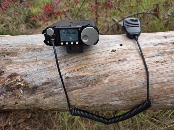 A Xiegu G106 radio on a fallen tree.