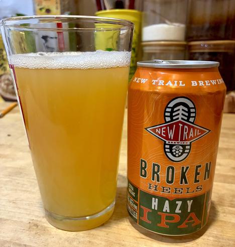 A glass is hazy golden beer in a pint glass and its orange can on the side.