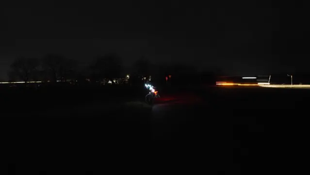 Bunt beleuchtetes Fahrrad auf einem Feldweg in der Nacht. Im Hintergrund verursacht ein Beleuchteter LKW Lichtspuren