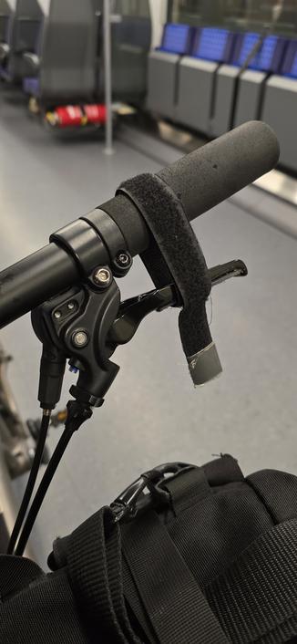 Bremsgriff an einem Fahrrad, um den schwarzes doppelseitiges Klettband gespannt ist. Im Vordergrund ist eine schwarze Tasche