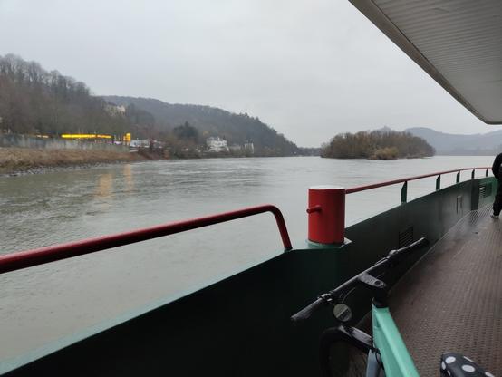 Ein Fahrrad auf einer Fähre, im Hintergrund der Rhein, die Insel Nonnenwerth und das Siebengebirge. An der Rheinuferstraße erkennt man eine Tankstelle.