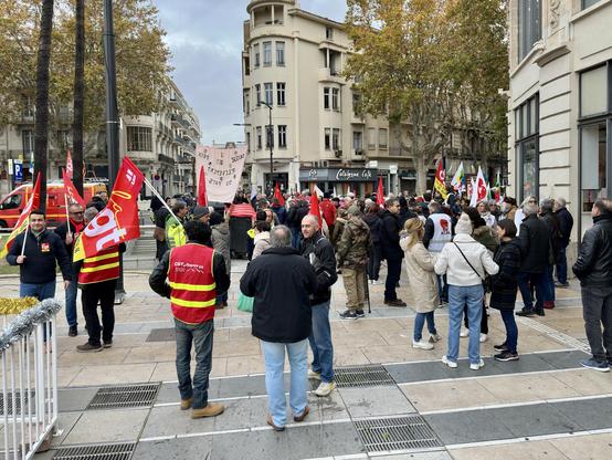 Un groupe de manifestants s'est rassemblé dans une zone urbaine, brandissant des drapeaux et des banderoles.