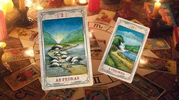 As cartas do baralho cigano “As Pedras” (à frente) e “A Cegonha” (atrás), sobre um fundo com motivos místicos. As cartas fotografadas tem arte gráfica de Cristina Martoni (2008), foram restauradas pelo ilustrador Lucas Teles Campos, e integram um baralho publicado originalmente por André Mantovanni/Editora Pensamento.