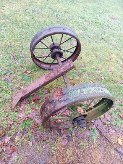 The two wheels now mounted on the same axle with the help of two steel pipe sleeves made from a fencepost and some other junk. A very rusty piece of C-beam is on top of it. It looks like it just got dug out of the earth, which is indeed the case.