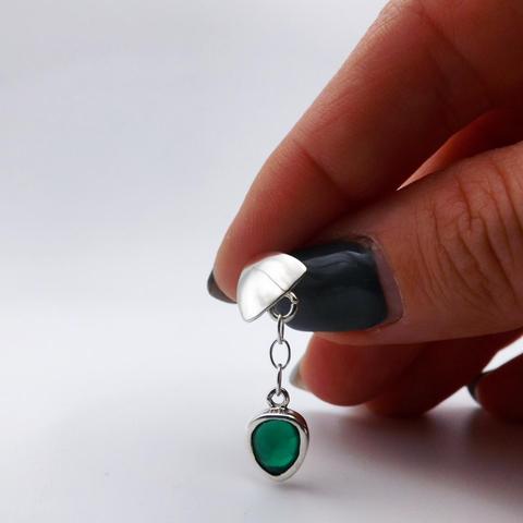 a silver earring with a green gemstone. it has a silver triangle and from there is connected with a small silver chain the gemstone. it's hold by a woman's hand