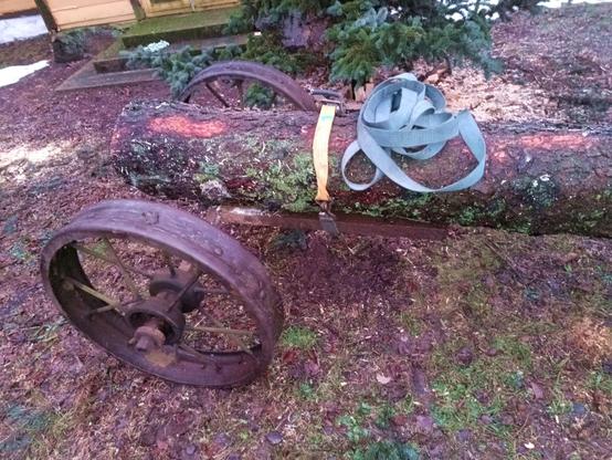 Log wheel with a log's thick end resting on the axle and secured with a ratchet strap to the c-beam so it stays in line with the log when making turns.