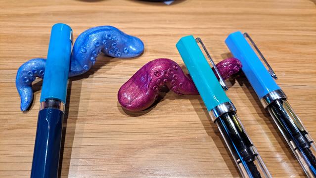 A pair of tentacle brush holders holding TWSBI fountain pens, two of which have transparent bodies that the ink can be seen through.