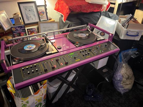 A purple disco console from the 1980s, with one turntable playing and the other waiting.