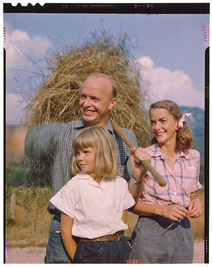 Photo showing a man, woman & girl all smiling with hay bales in the background from Toni Frissell's New England Characters series. This photo is titled "NewEnglandCharactersSeptember 1947" and shows a rural setting with clear blue skies above. The people depicted are likely from New England states as per context provided.